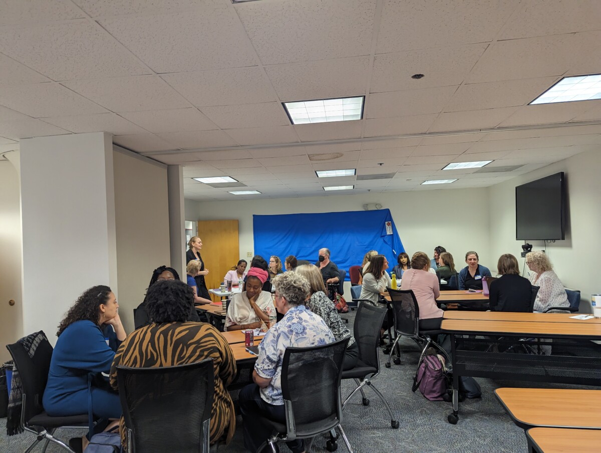 About 20 staff members can be seen in the training room, sitting at tables for group discussions.